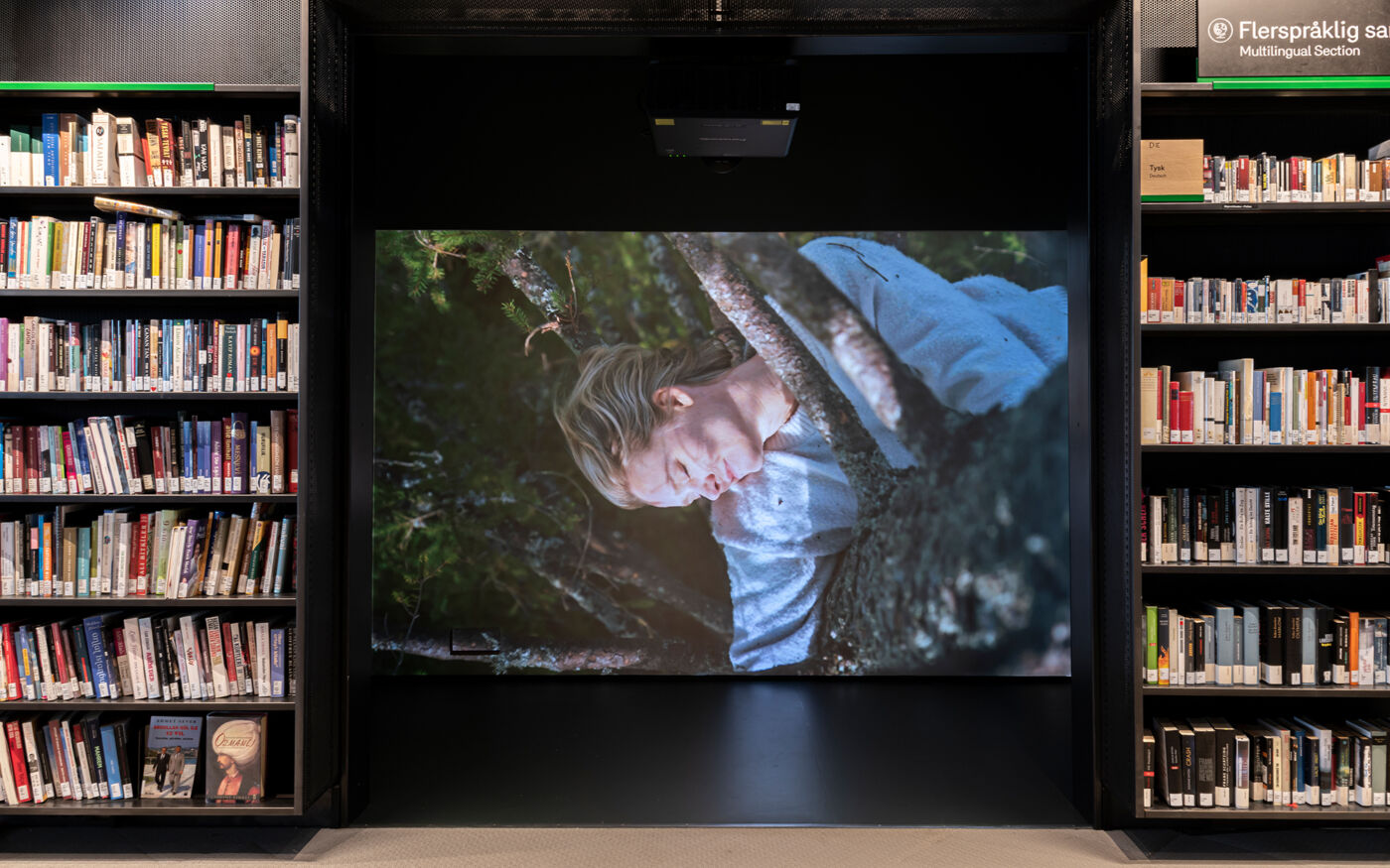 Bilde viser projisering av film på skjerm i biblioteket, i et avlukke flankert av bokhyller. Foto