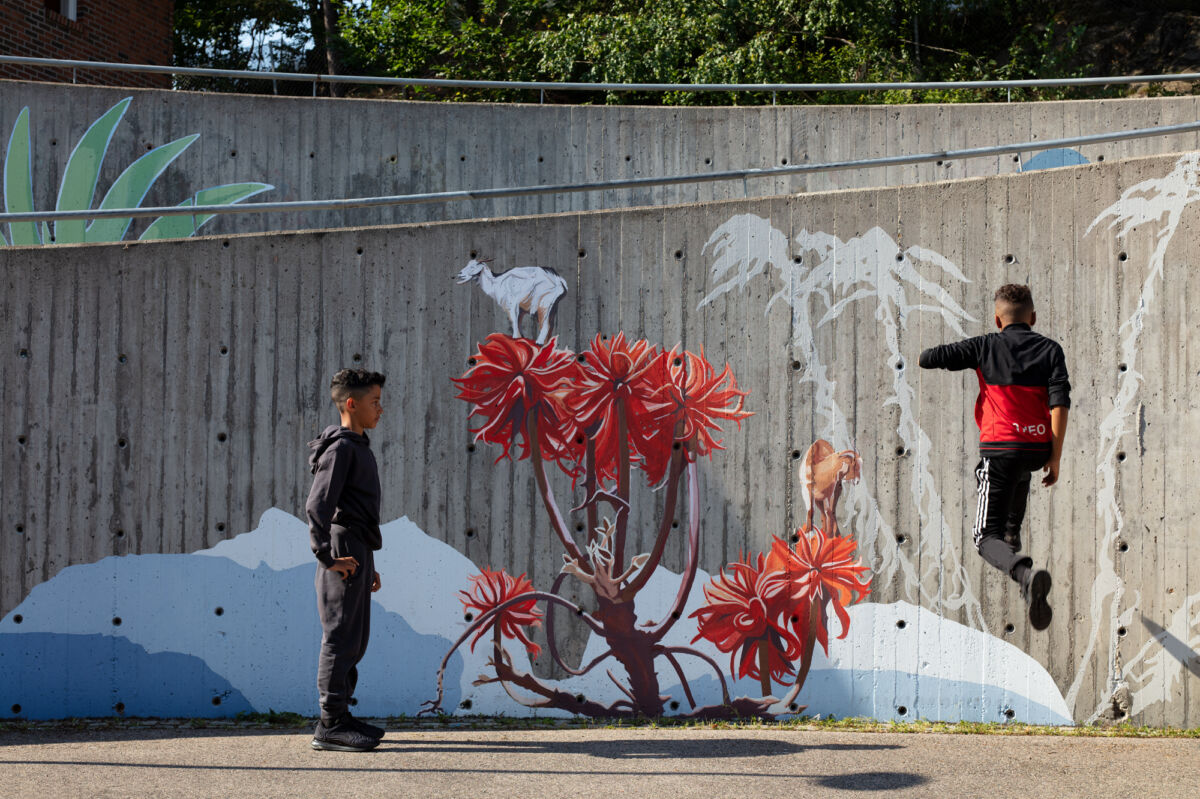 Two kids in front of a colorful murial painting in a schoolyard. Photo