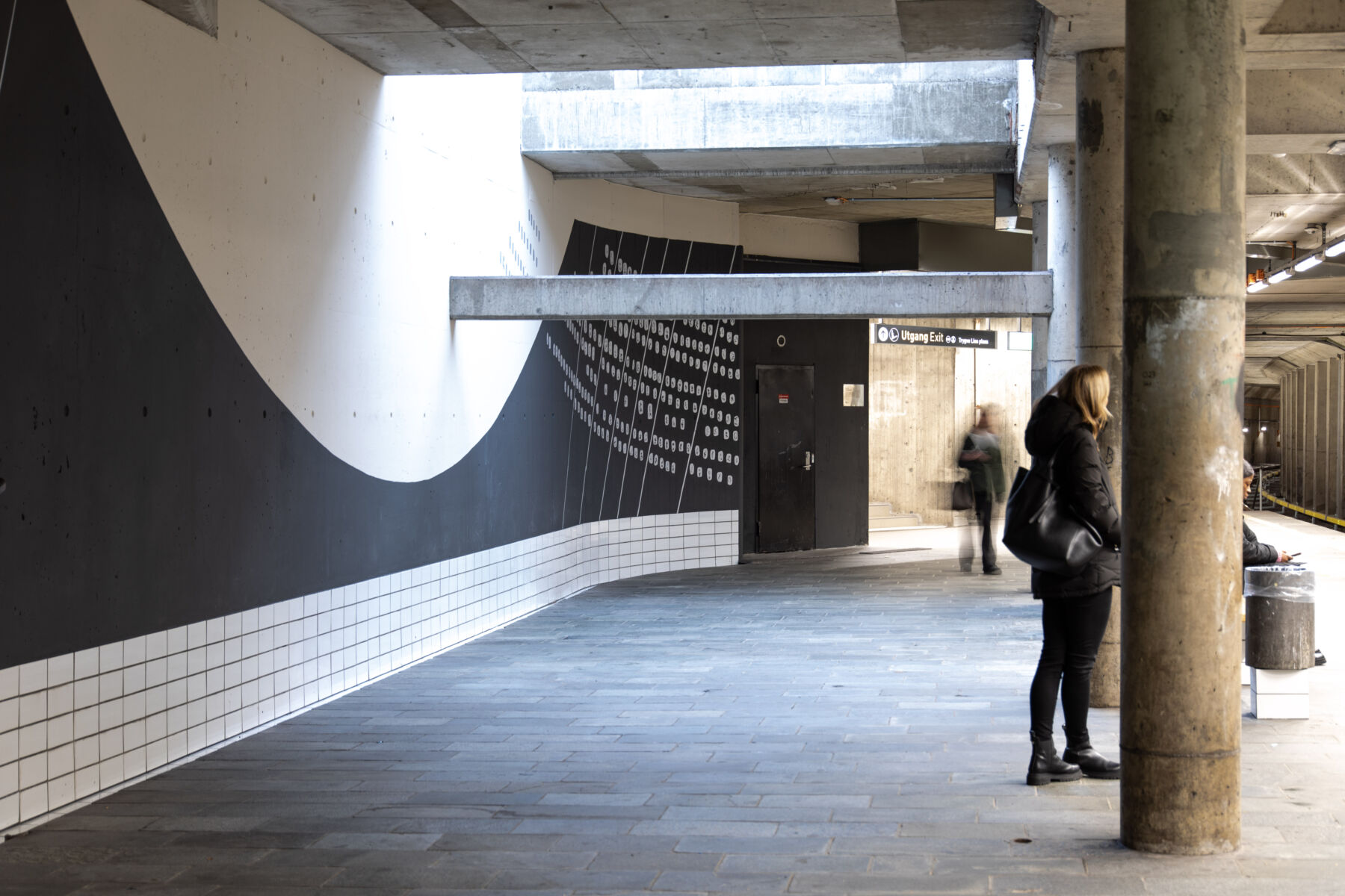 T- banestasjon, kunstverk oppmalt på vegg, mennesker venter å perrongen. Foto