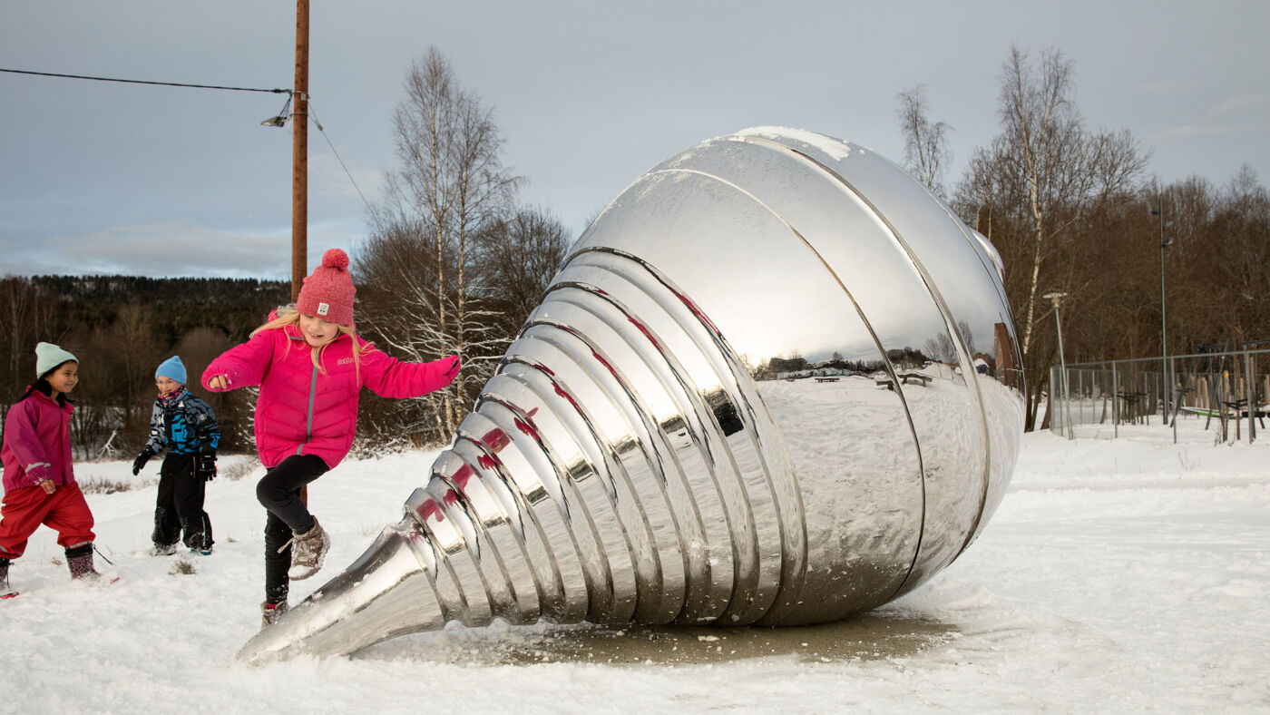 Foto av barn som løper rundt en skulptur av en stor snurrebass.