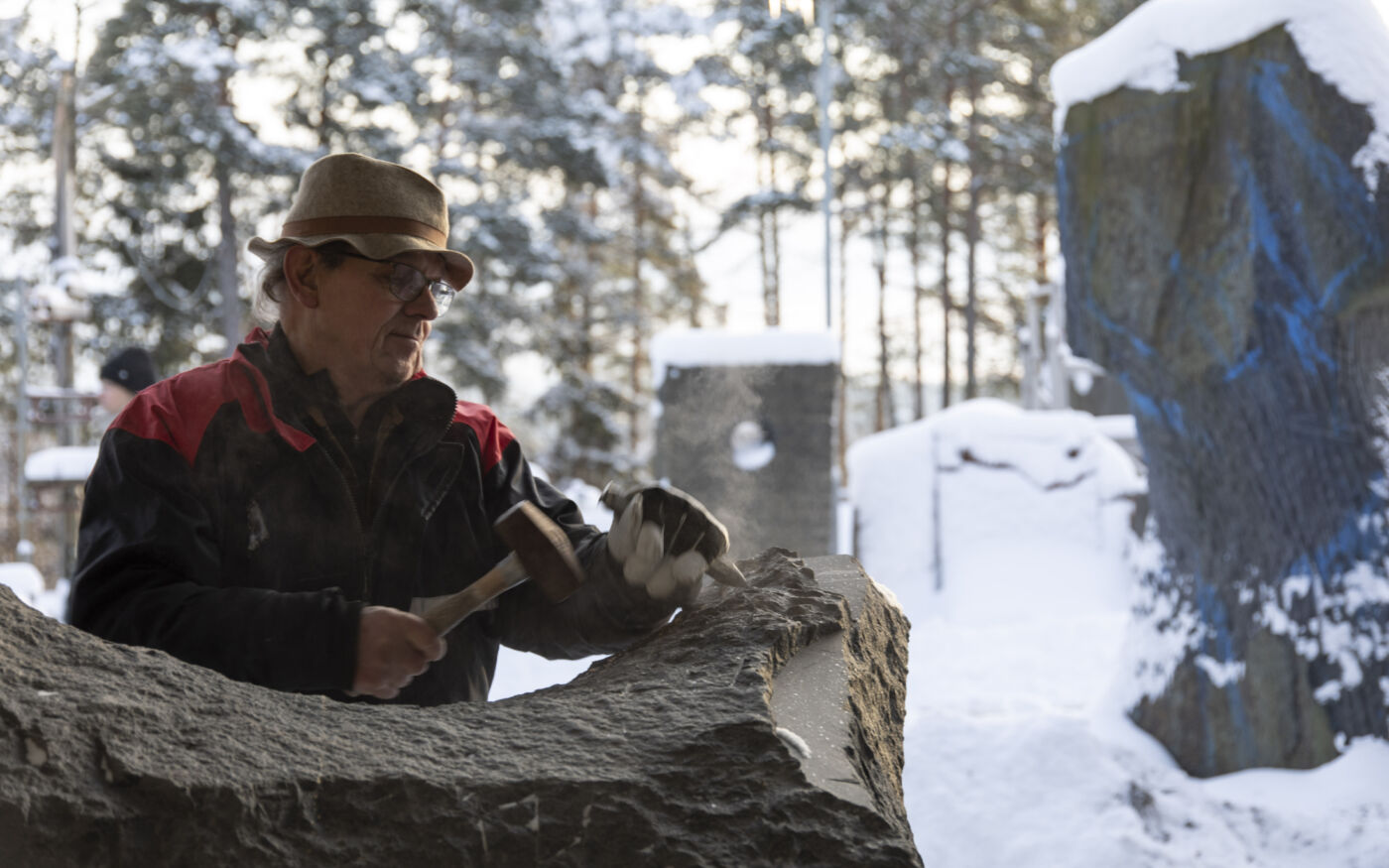 Kunstner Kristian Blystad hugger i stein i sitt uteatelier, nærbilde. Foto