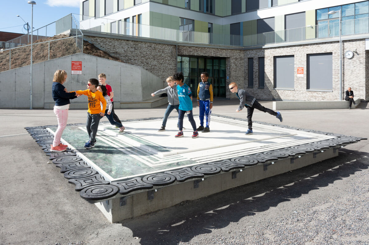 Foto av stenskulptur formet som et stort bord i en skolegård, med elever som leker oppå.