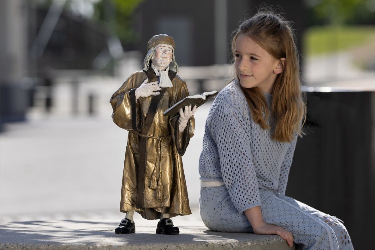 Foto av barn som sitter ved siden av skulptur som viser Per Aabel.