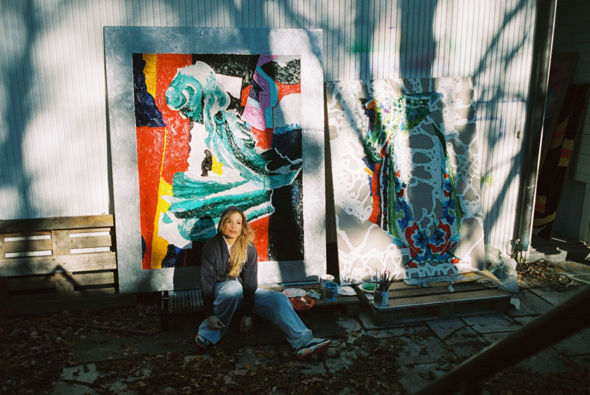 Foto av kunstner Ida Ekblad foran to kunstverk stående mot en vegg.