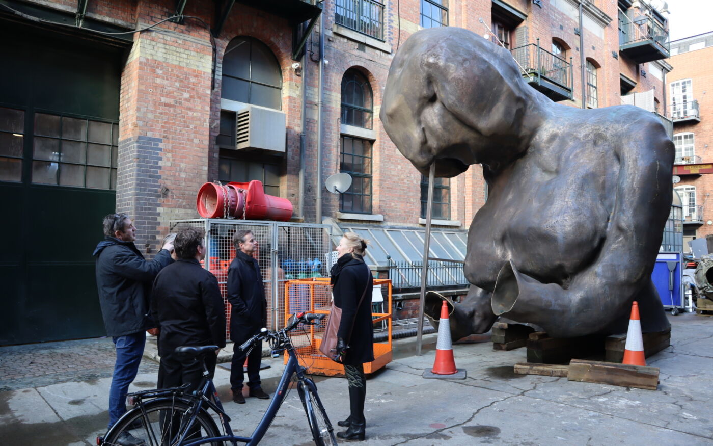 Del av skulptur, torso står ute på bakken, en gruppe mennesker står i forgrunnen. Foto