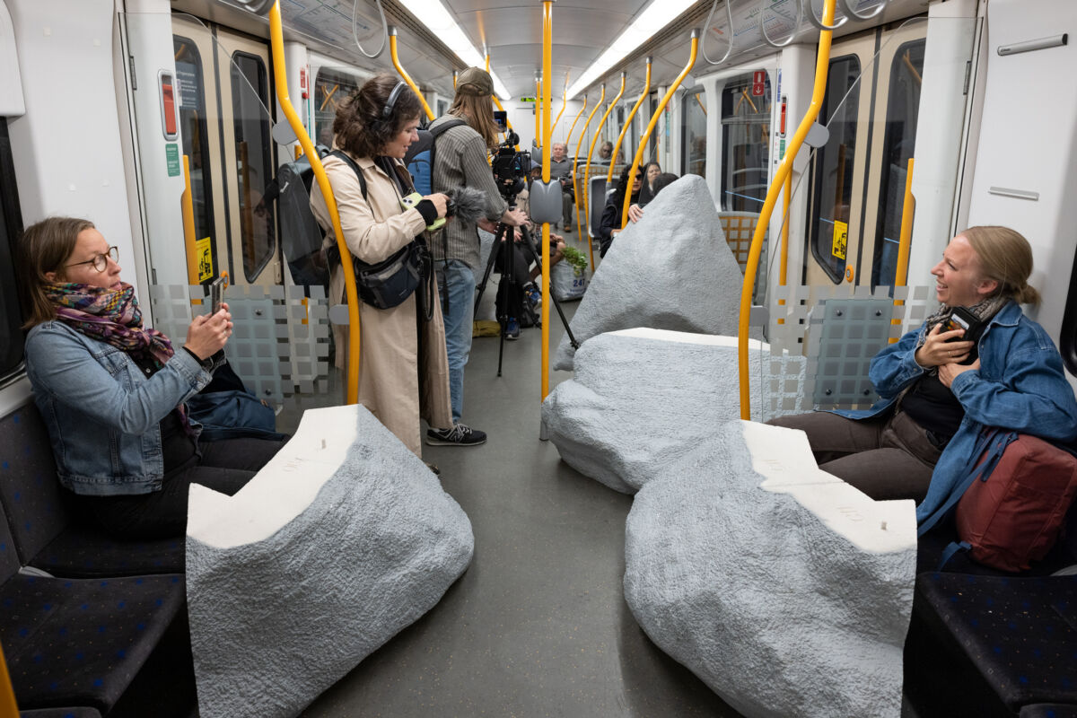 Foto av en t-banevogn fylt med mennesker og deler av steinskulptur.