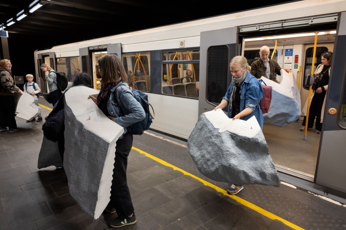 Personer går av t-banen mens de bærer på deler av steinskulptur. Foto