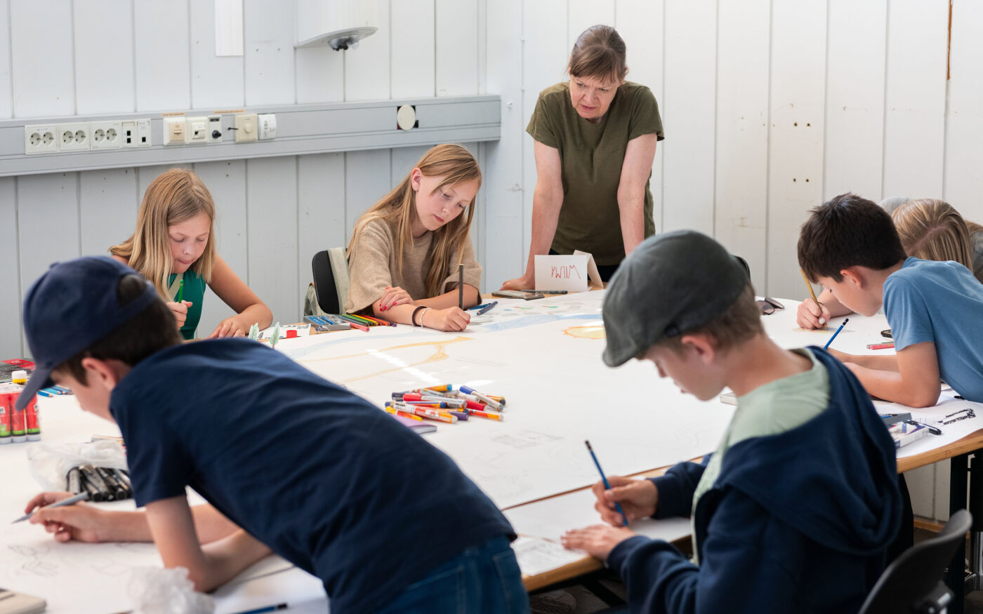 Foto av barn og unge som jobber i et kunstverksted sammen med en lærer.