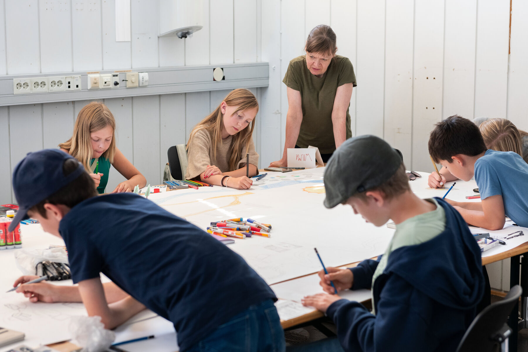 Foto av barn og unge som jobber i et kunstverksted sammen med en lærer.