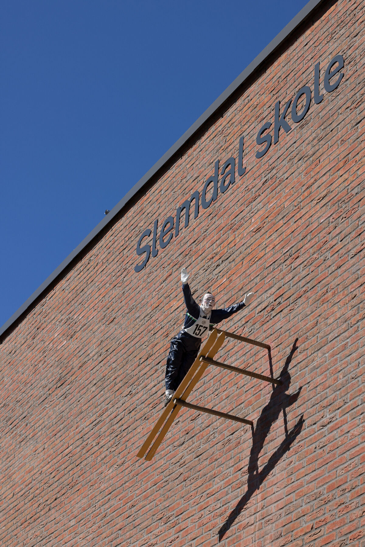 Foto av en skulptur av en skihopper som henger på fasaden til Slemdal skole.