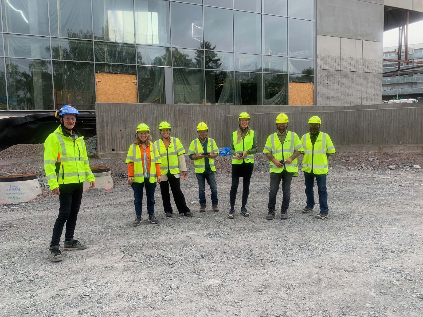 Foto av sju mennesker med refleksjakker og hjelm på en byggeplass.