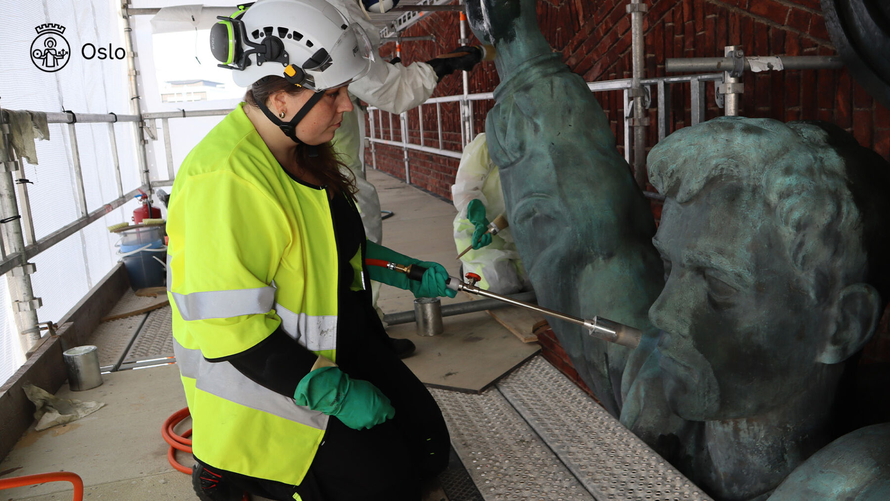 Foto av person som konserverer St. Hallvard-skulpturen på Rådhusets fasade.